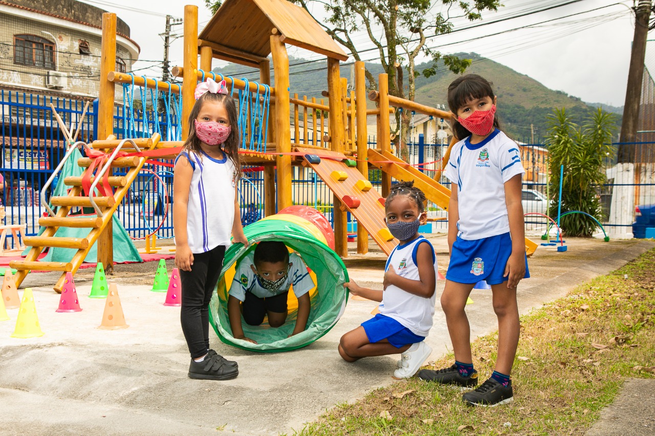 Foto de crianças usando uniforme e máscara brincando no parquinho