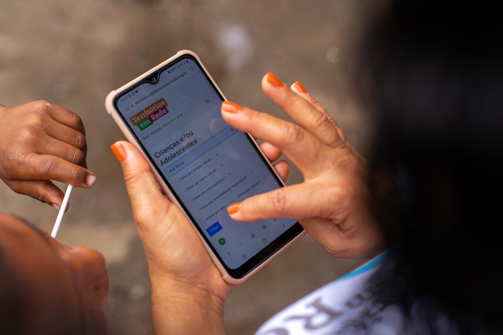 A female hand with orange nail polish is registered in the "Territories in Network" application while a child with a lollipop in his mouth watches the action.