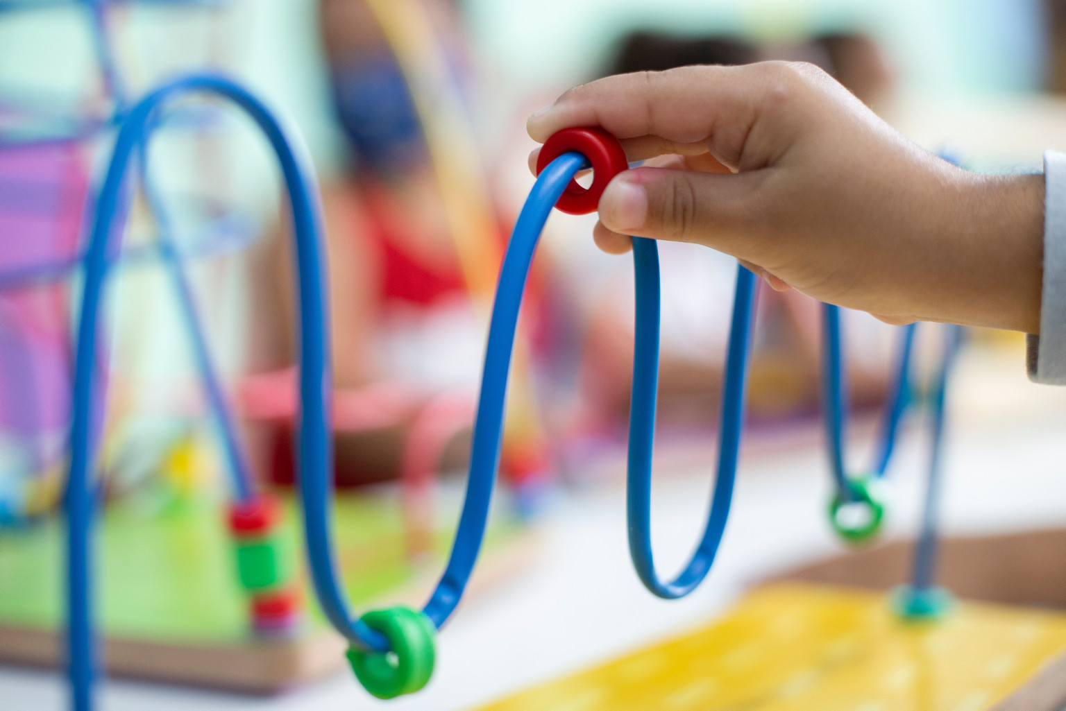 Mão de uma criança brincando em um brinquedo que consiste passar pequenas argolas de plástico em um tubo com curvas. 